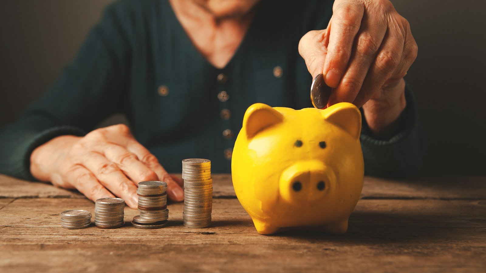 Elderly hands depositing coins into a yellow piggy bank
